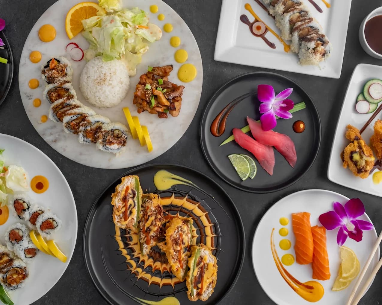 Spread of sushi rolls, nigiri, salmon sashimi and a teriyaki plate on several dishes at Rolling Rice