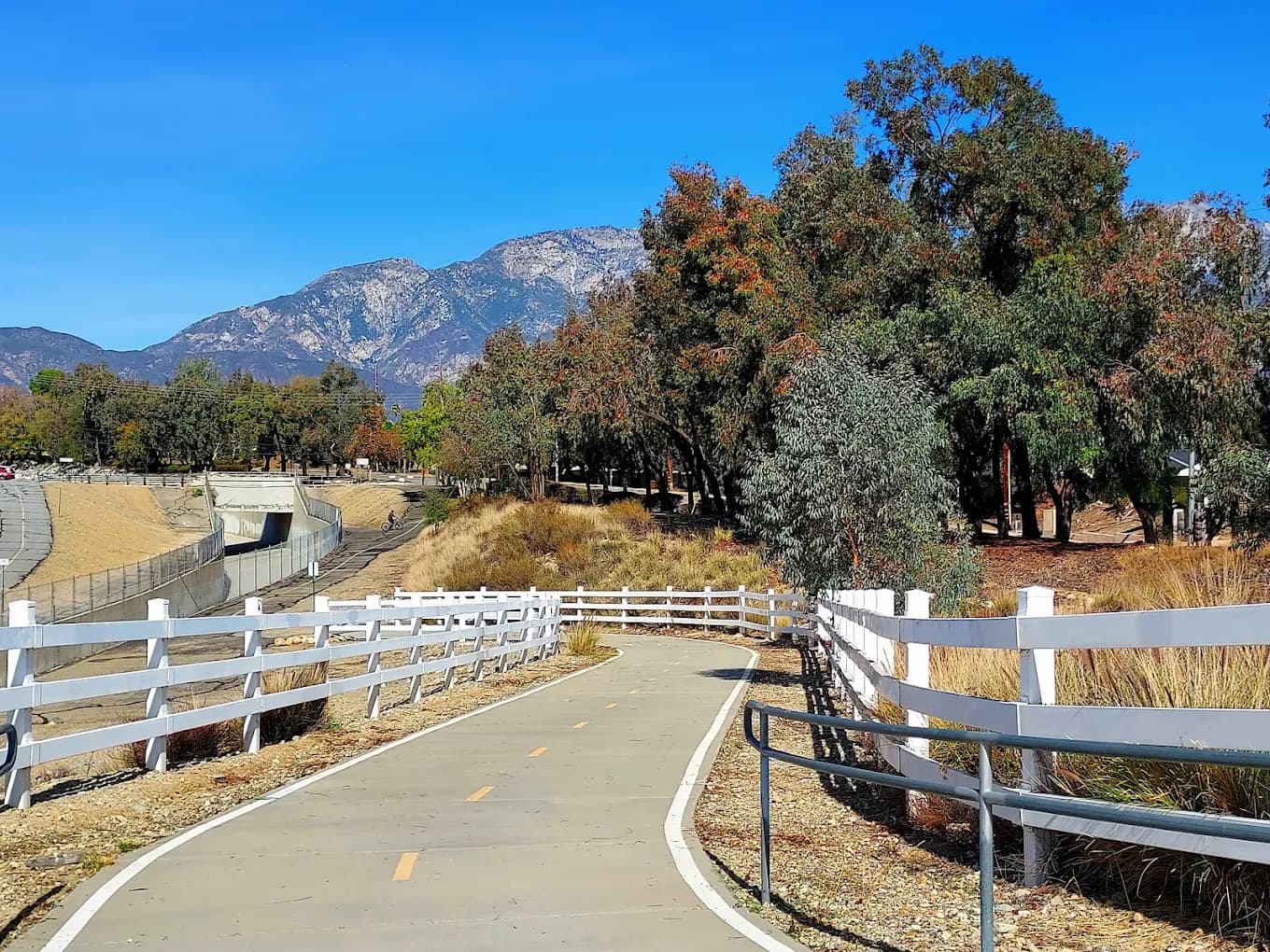 Paved bike path with white rail fencing at Route 66 Trailhead Park, mountains in the background