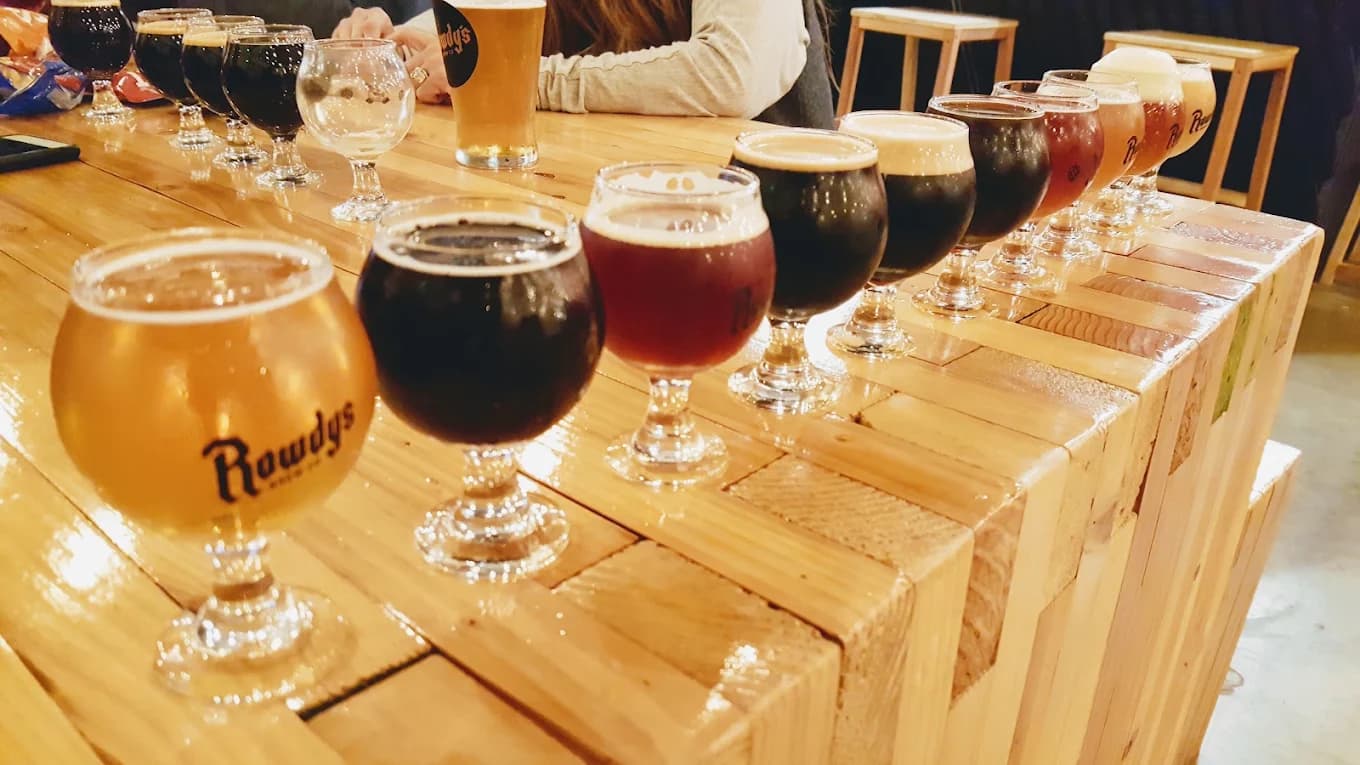 Row of tulip glasses filled with beers of different colors along a wood bar at Rowdy's Brew Co