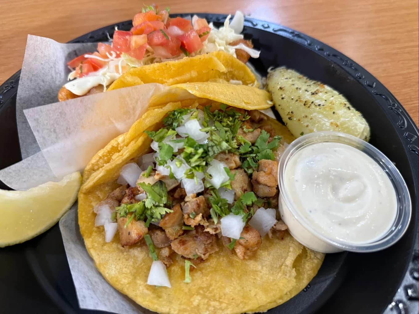 Chicken taco with onion and cilantro, a fish taco with pico de gallo, a lime wedge and crema on a plate at Senor Baja