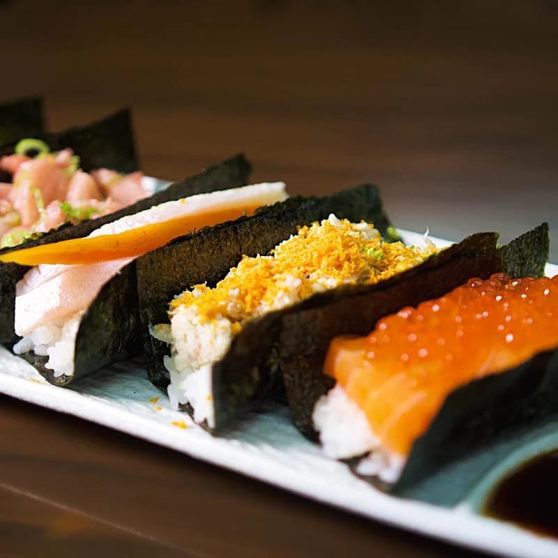 Row of hand rolls with salmon roe, crab and yellowtail on a long white plate at Shokunin
