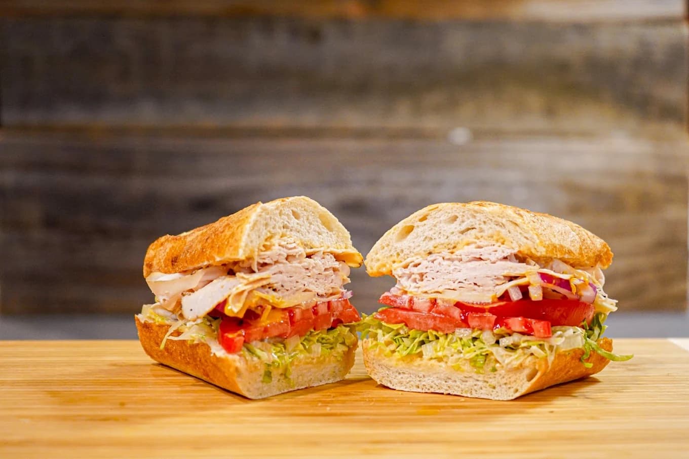 Turkey sandwich with lettuce, tomato and onion cut in half on a wooden board at Sourdough & Co
