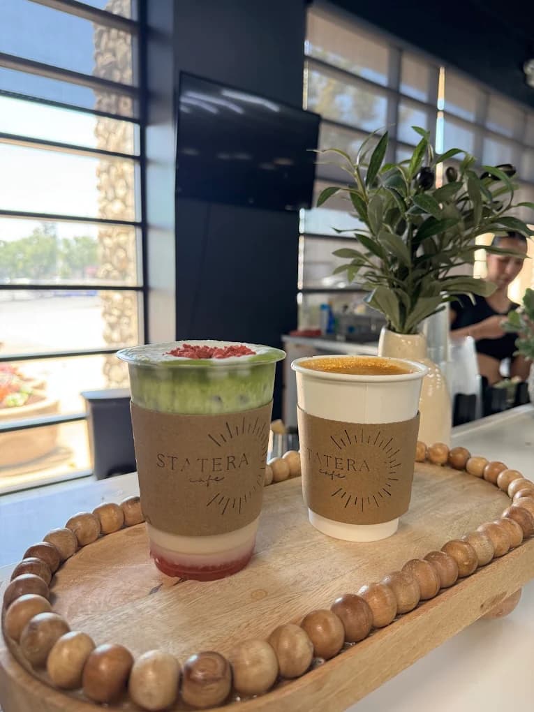 Iced matcha latte and a hot drink in branded Statera Café sleeves on a beaded wooden tray