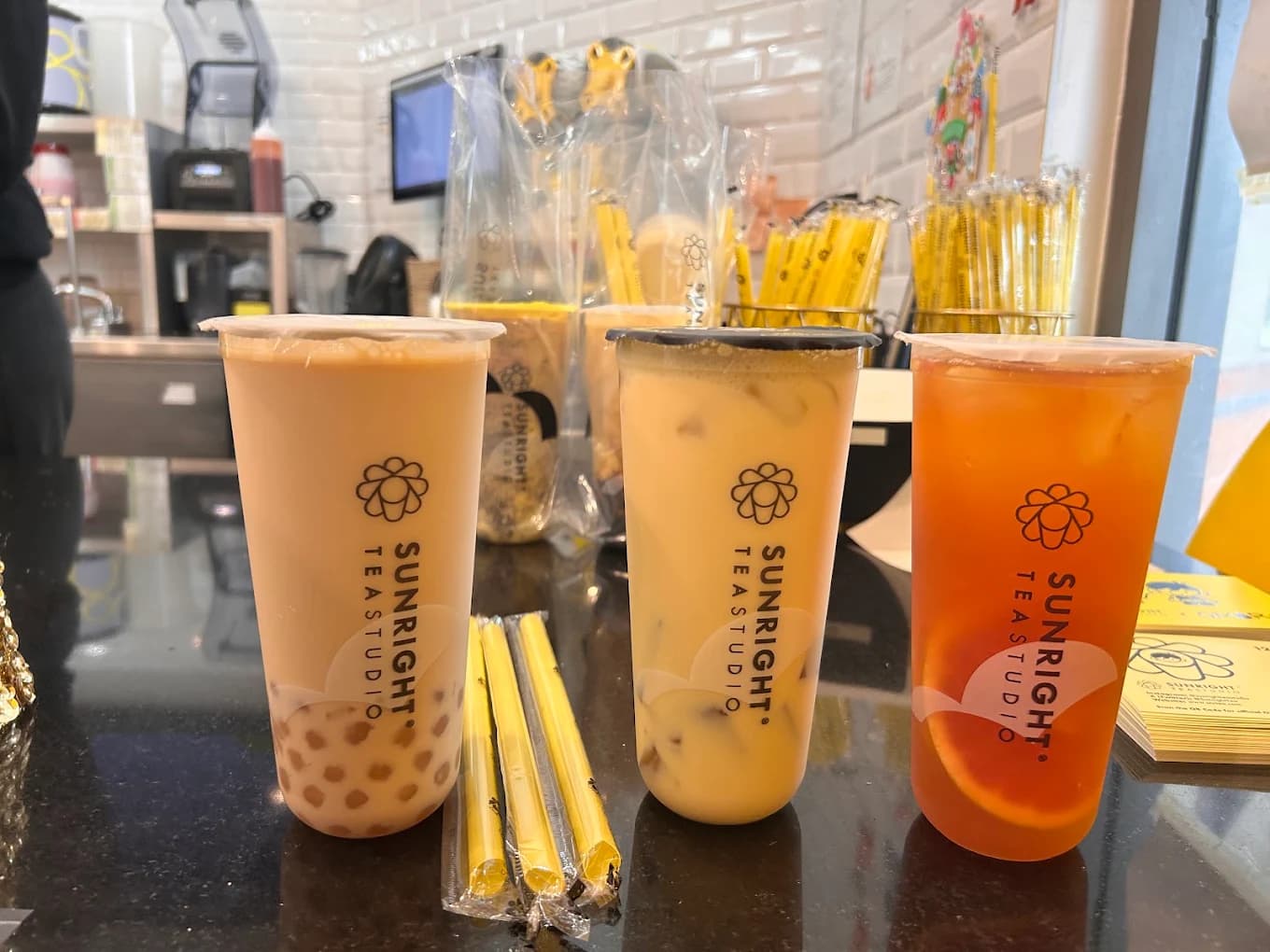 Three iced teas in Sunright Tea Studio cups, including boba milk tea, lined up on a counter