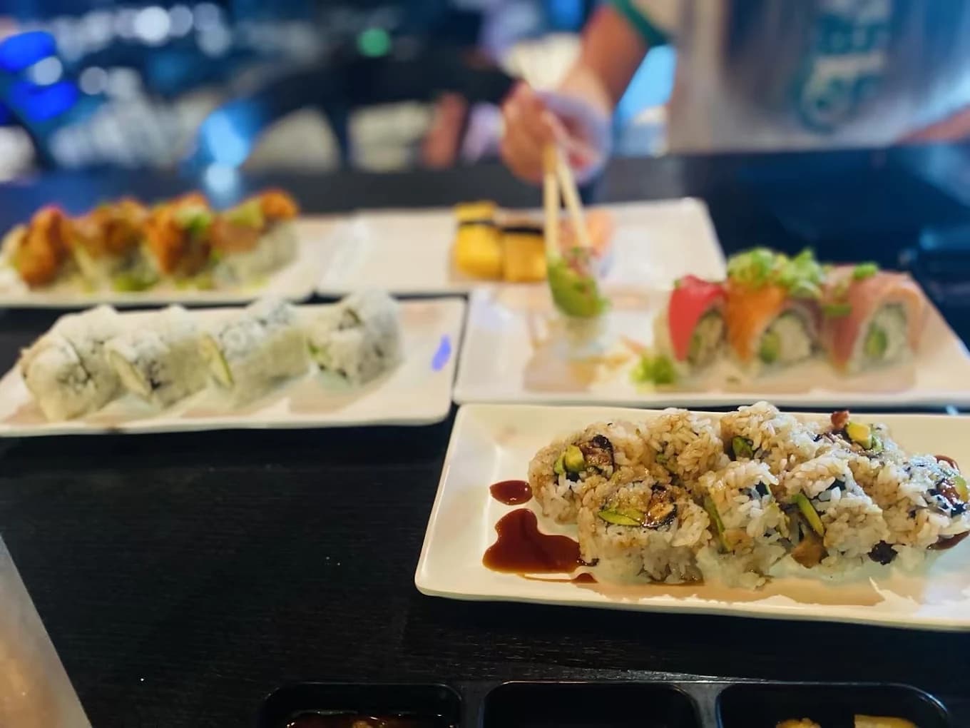 Several plates of sushi rolls, including a rainbow roll and eel roll, on a dark table at Sushi Martini