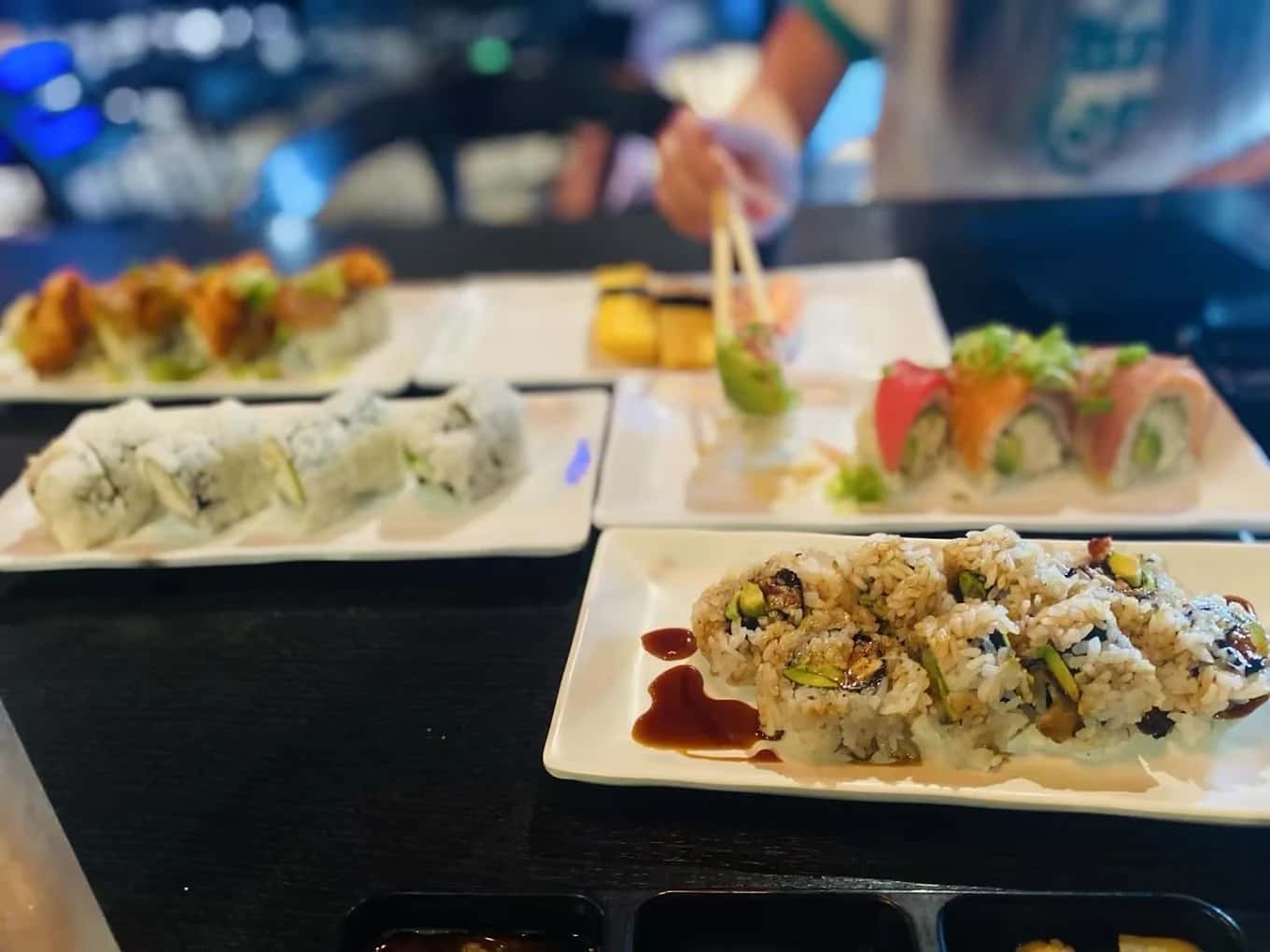 Several plates of sushi rolls, including a rainbow roll and eel roll, on a dark table at Sushi Martini