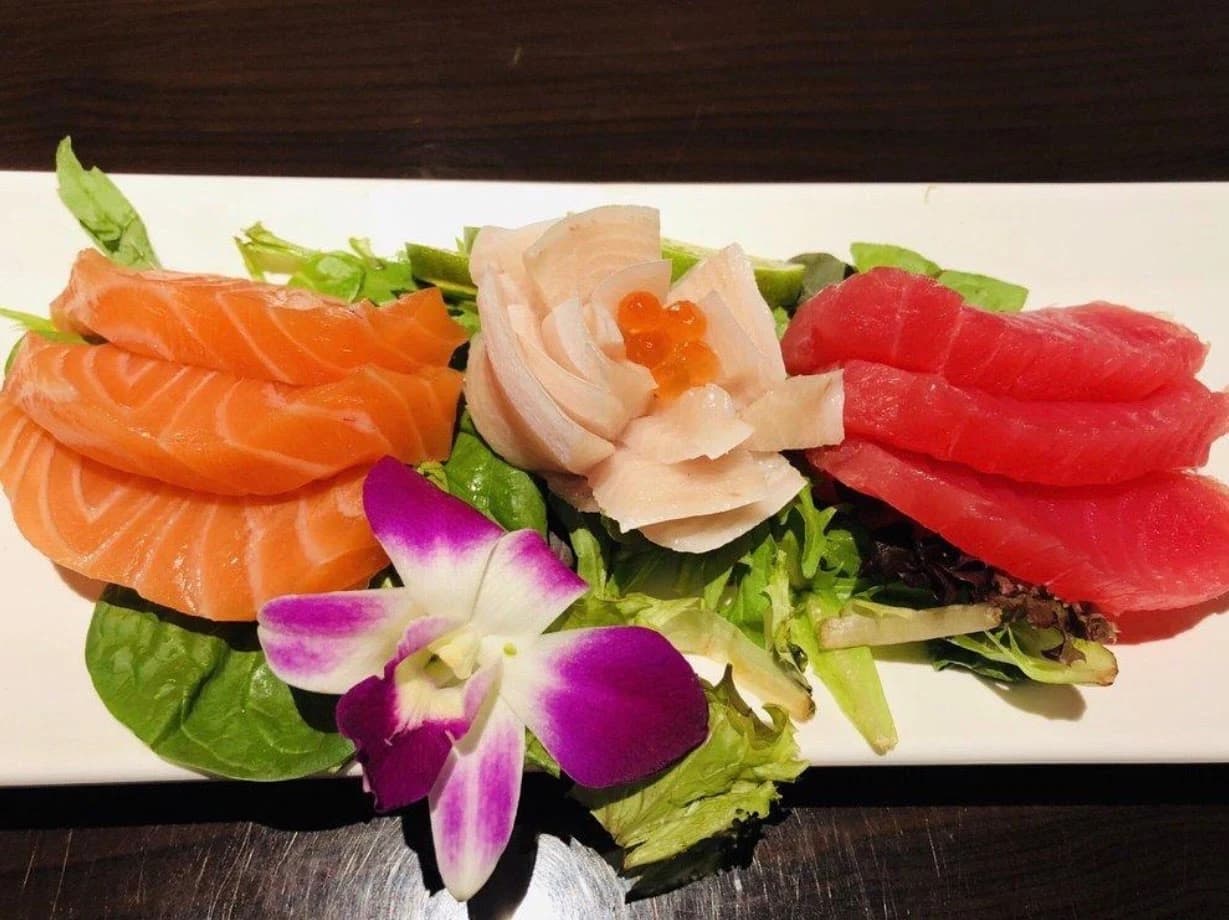 Sashimi platter of salmon, tuna and white fish over greens with a purple orchid at Sushi One Spot