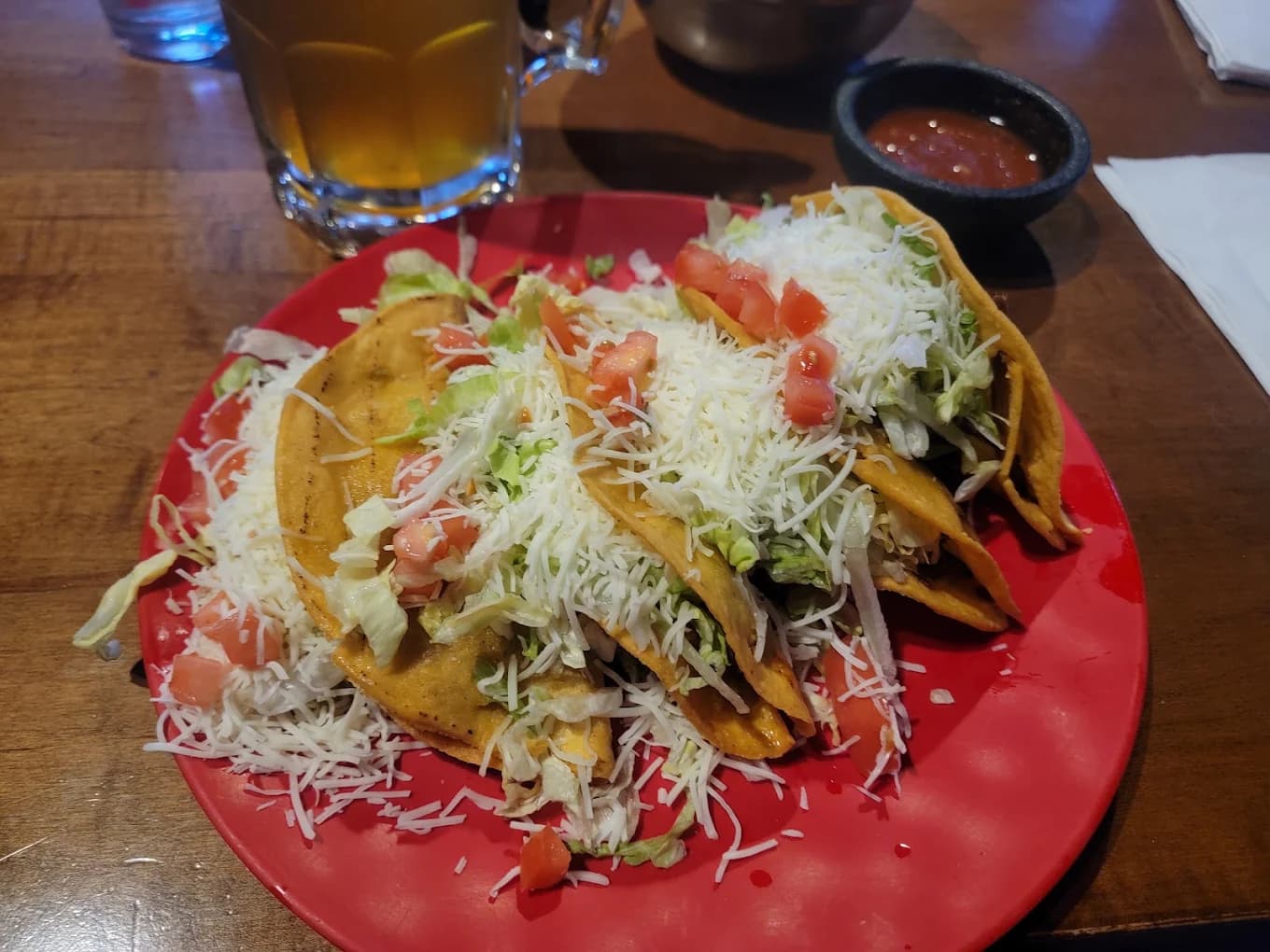 Crispy tacos topped with shredded cheese, lettuce and tomato on a red plate at Taco Hut