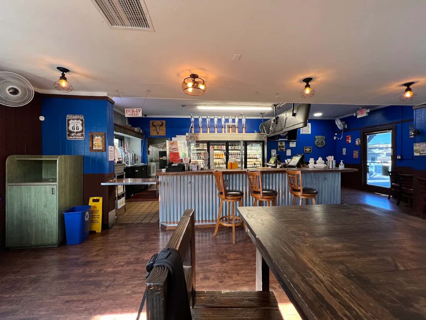 Dining room at Tacos Los Carnales with blue walls, Route 66 signs, a corrugated-metal bar and wood tables
