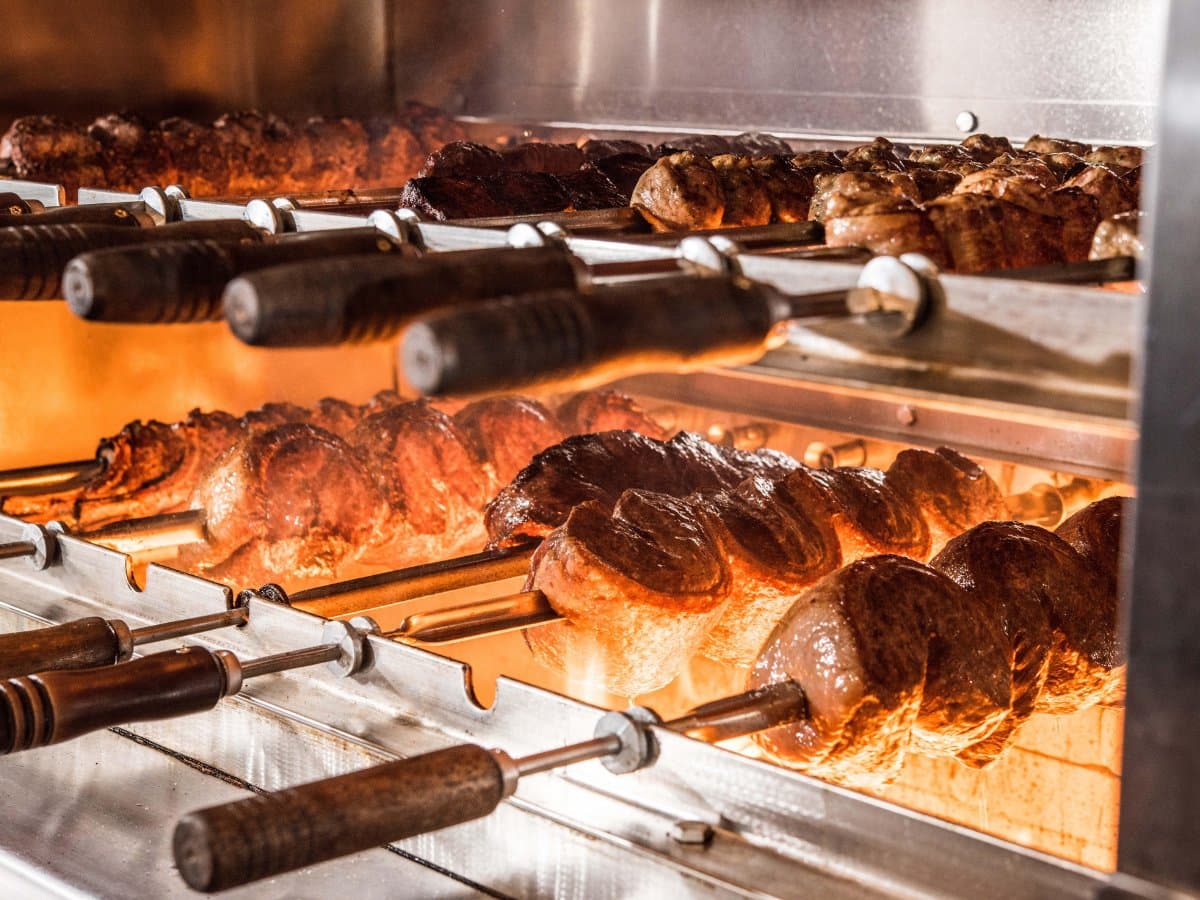 Skewers of meat roasting over glowing coals on the rotisserie grill at Texas de Brazil