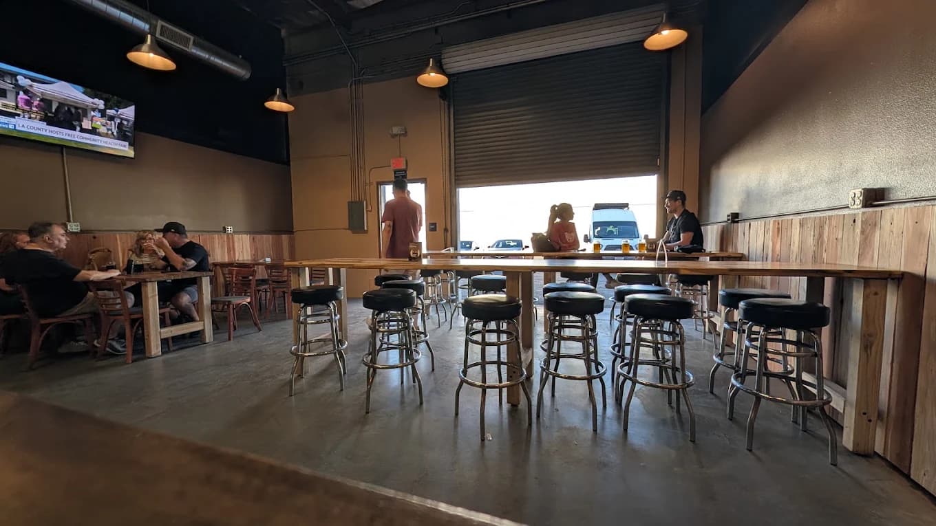 Taproom at The Brewmill with long wooden tables, black bar stools and an open roll-up door