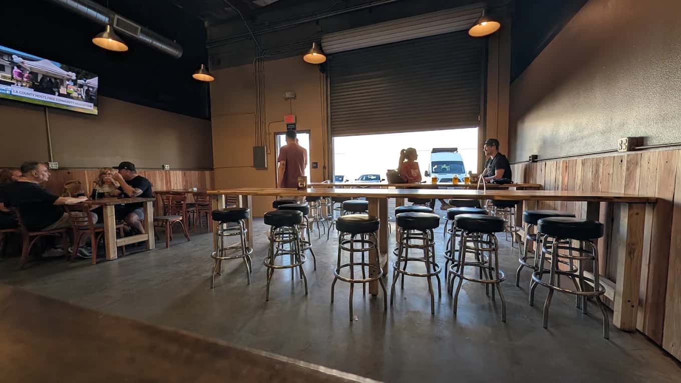 Taproom at The Brewmill with long wooden tables, black bar stools and an open roll-up door