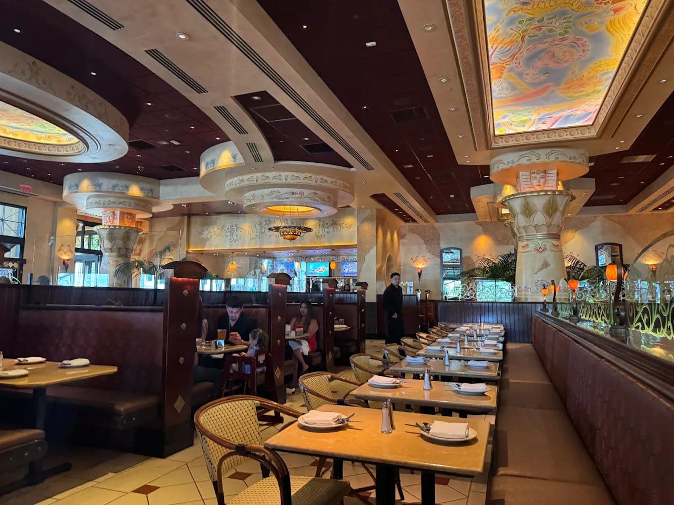 The dining room at the Cheesecake Factory, booths and set tables beneath painted columns and a domed ceiling