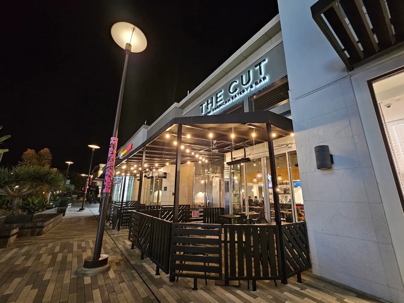 Night exterior of THE CUT Modern American Eatery & Bar with a lit sign and string-light patio