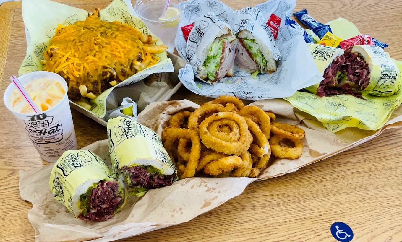 A tray of pastrami dip sandwiches in wax paper with chilli cheese fries and a heap of onion rings