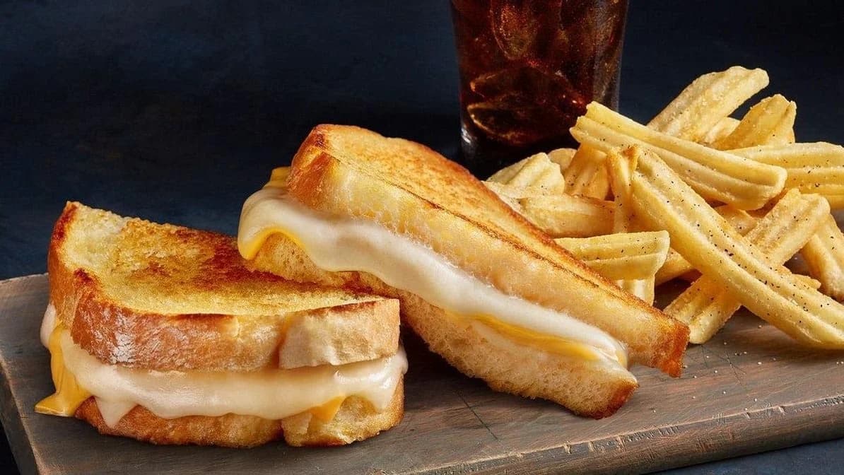 Grilled cheese sandwich halves with waffle fries and a soda on a wooden board from The Meltdown