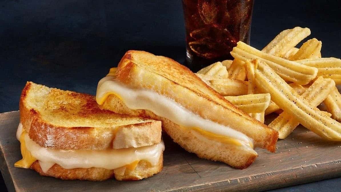 Grilled cheese sandwich halves with waffle fries and a soda on a wooden board from The Meltdown