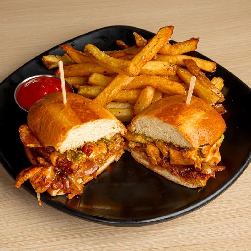 Halved chicken sandwich with fries and ketchup on a black plate from The Original Hills Kitchen