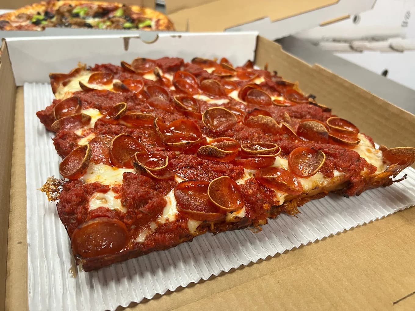 Square pepperoni pizza with cupped pepperoni in a takeout box from The Parlor Pizzeria