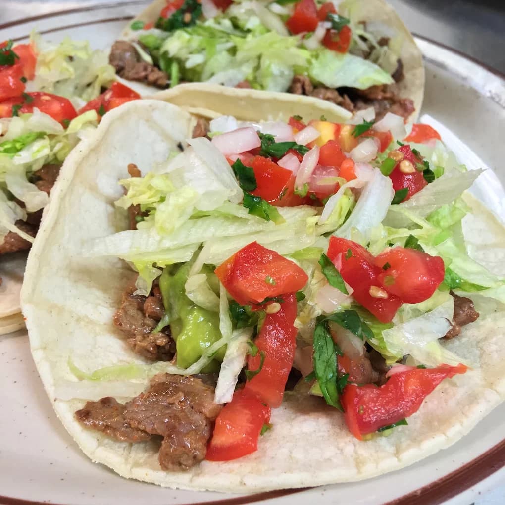 Carne asada tacos on corn tortillas with lettuce, tomato and guacamole from Tio's Mexican Food