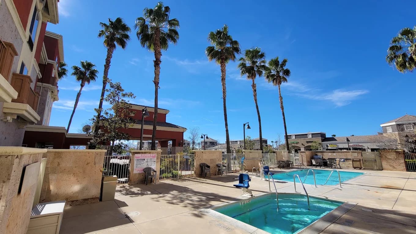Pool and hot tub at TownePlace Suites Ontario Airport, ringed by a metal fence and tall palm trees under a blue sky