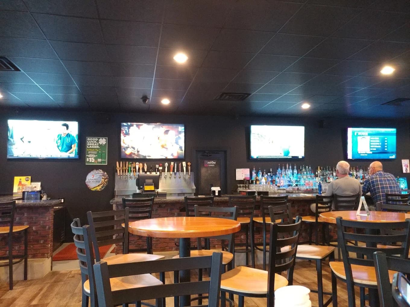 Bar room at 210 Tavern with wood tables, metal chairs, beer taps and TVs above a brick-front bar