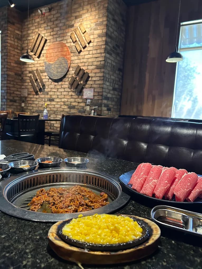 Tabletop grill at U Grill Korean BBQ with marinated meat, sliced beef, corn cheese and a brick wall behind