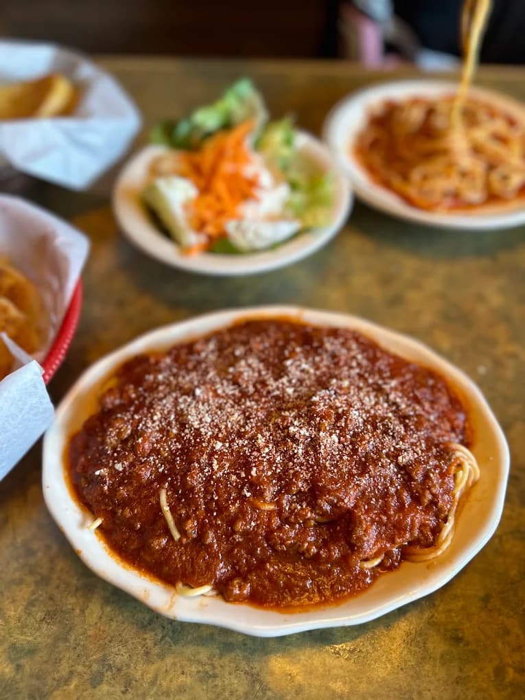 Plate of spaghetti with meat sauce and grated cheese at Vince's Spaghetti, salad and bread behind