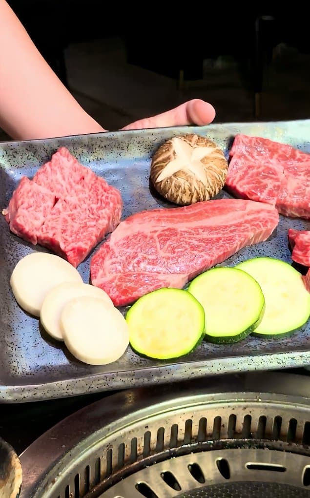 Platter of raw marbled beef, mushroom, zucchini and onion beside a tabletop grill at Wagyu Factory