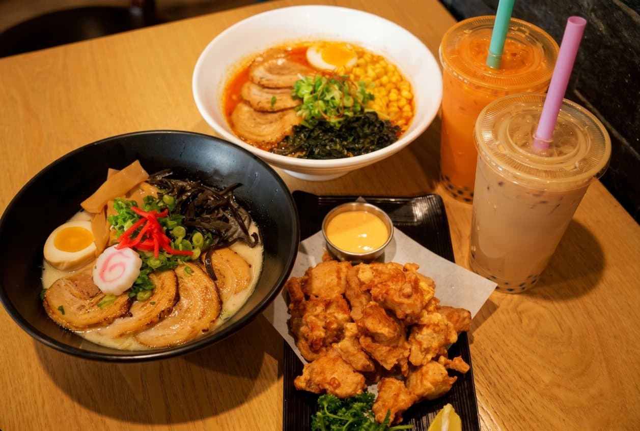 Two bowls of ramen, fried chicken karaage and two iced boba drinks on a table at Wazakuraken Ramen