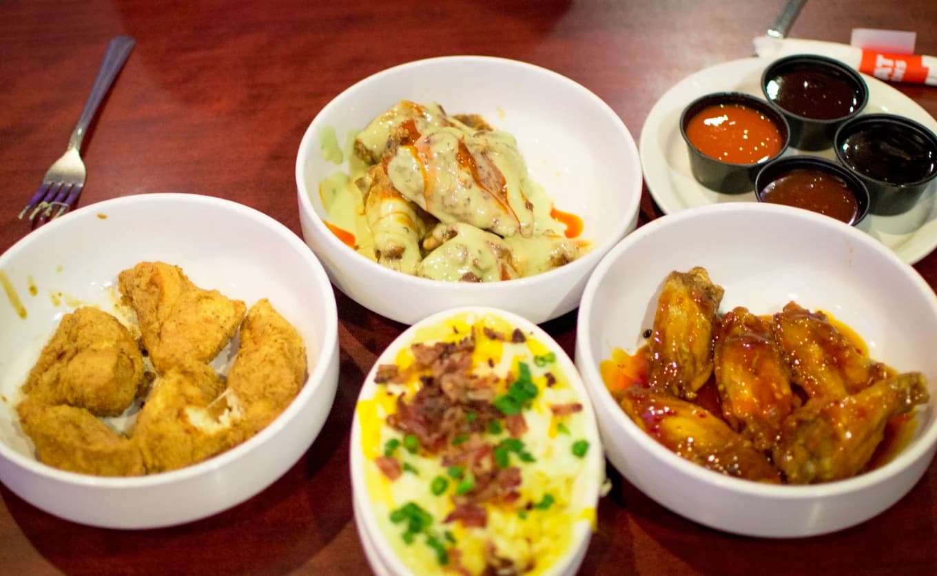 Bowls of breaded and sauced chicken wings with loaded mashed potatoes and dipping sauces at Wings and Rings