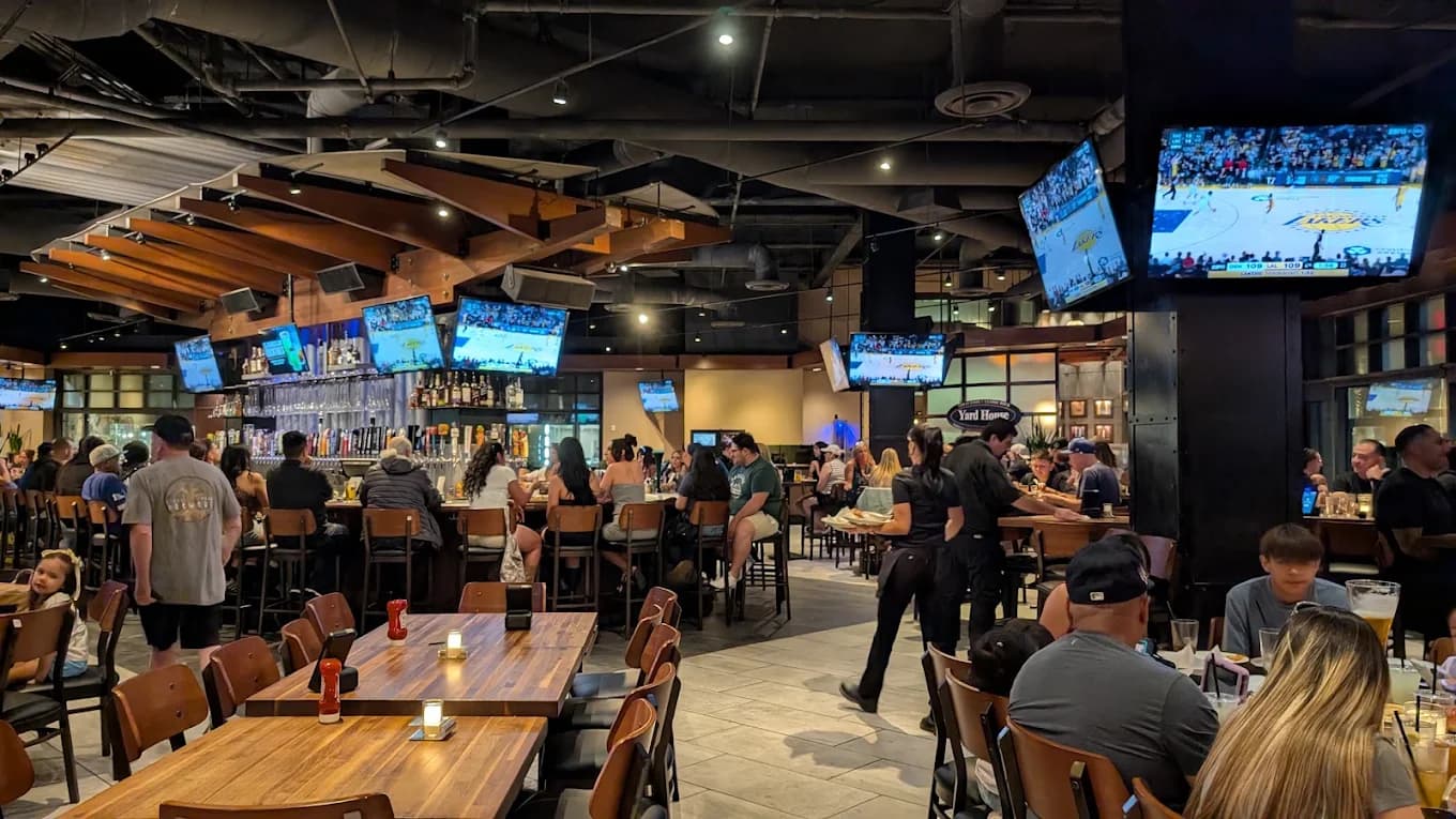 Crowded dining room and bar at Yard House with wood tables and rows of TVs showing basketball